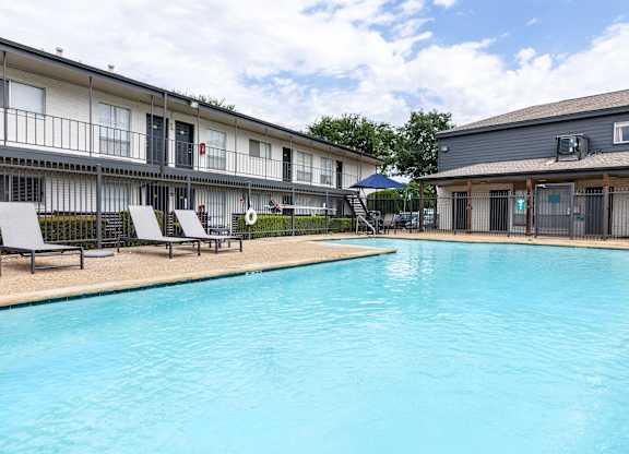 A swimming pool in front of a building with lounge chairs around it.