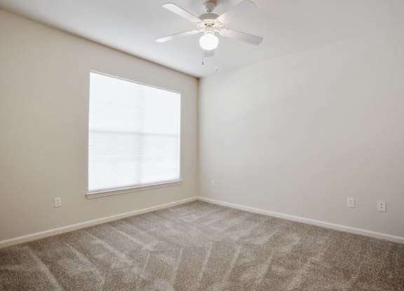 A room with a ceiling fan and a large window at Addison Park Apartments in Arlington, TX.