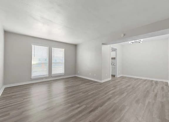 A spacious room with wooden flooring and two windows.