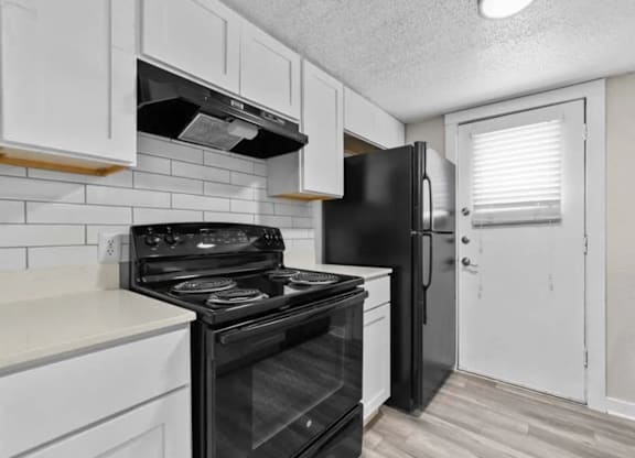 A black refrigerator sits in a kitchen with white cabinets.