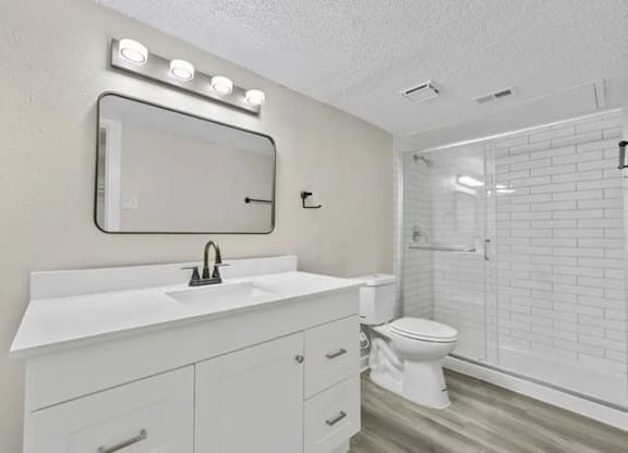 A white bathroom with a sink, mirror, and toilet.
