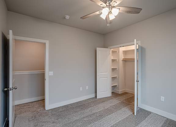 A room with a ceiling fan and two open doors at Cedar Crest Apartments, Farmington 72730