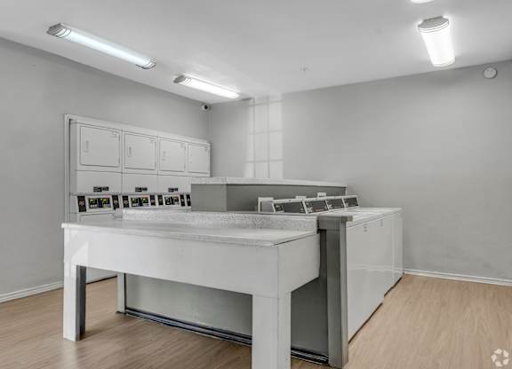 A white table with a grey countertop and a white cabinet with drawers is in a room with white walls and wooden flooring.