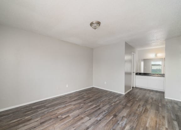 an empty living room with wood flooring and a kitchen at Helios, Dallas, TX 75240