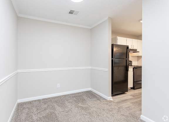 an empty room with white walls and a kitchen with a black refrigerator