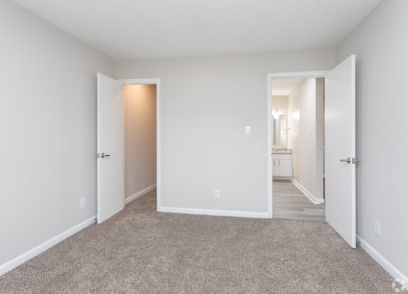 a bedroom with white walls and carpet and a hallway to a bathroom