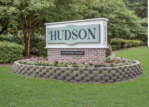 The sign for Hudson Apartments in a grass field and trees