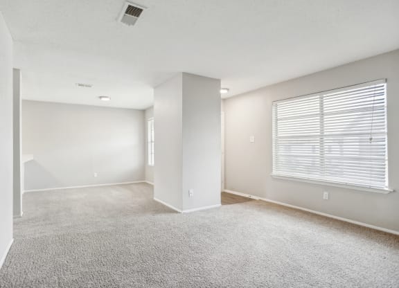 the spacious living room and dining room of an apartment with white walls and carpet