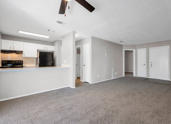 an empty living room with a kitchen and a ceiling fan