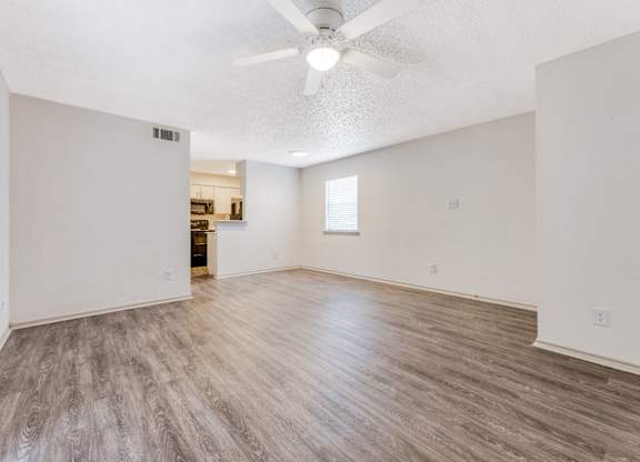 an empty living room with a ceiling fan and a kitchen