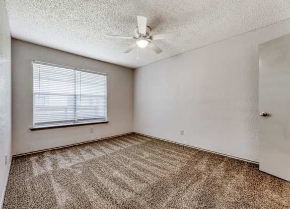 an empty bedroom with a ceiling fan and a window