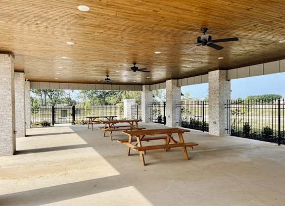 A covered patio with wooden picnic tables and a ceiling fan at Cedar Crest Apartments, Farmington, Arkansas