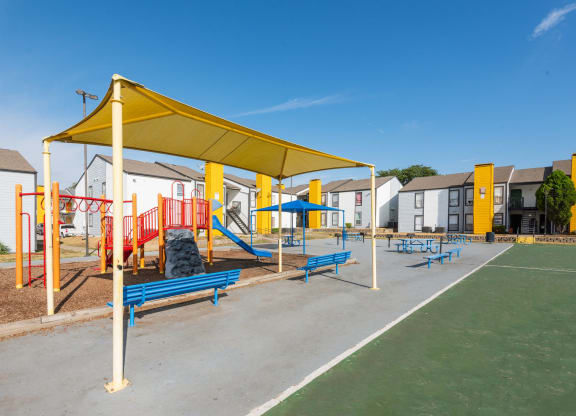 a playground with benches and a yellow canopy in front of apartment buildings at Helios, Dallas, TX