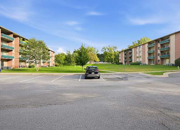A black car is parked in a parking lot in front of apartment buildings.