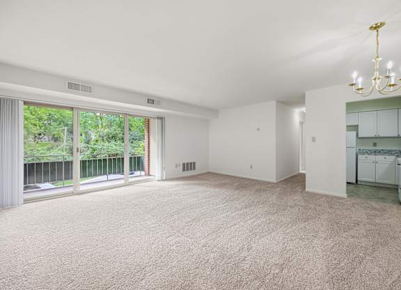 A spacious living room with a carpeted floor and a chandelier hanging from the ceiling.