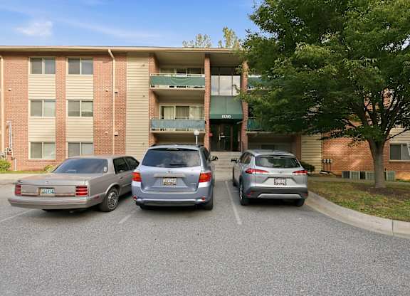 Three cars parked in front of a brick apartment building.