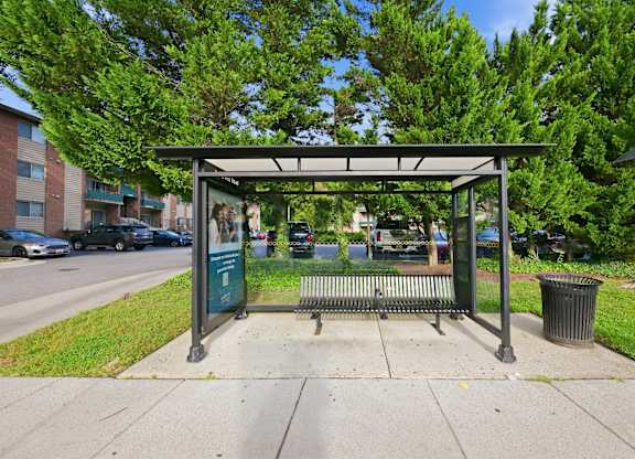 A bus stop with a bench and a shelter is located on a sidewalk.