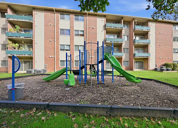 A playground with a green slide in front of a brick apartment building.