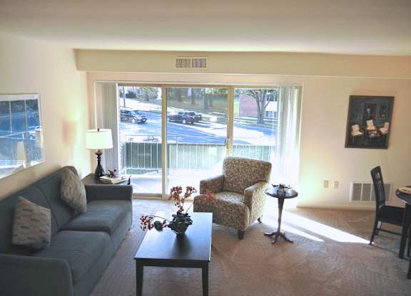 A living room with a couch, chair, and a table with a vase of flowers on it.