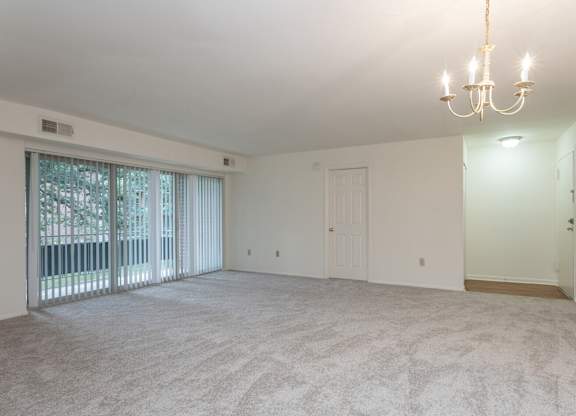 A large, empty room with a chandelier and sliding glass doors.