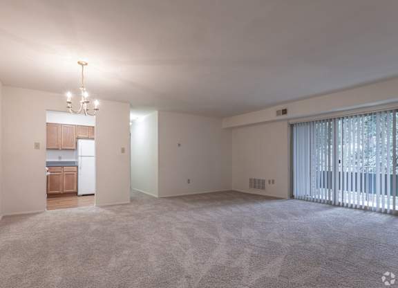 A spacious living room with a kitchen in the background and a carpeted floor.