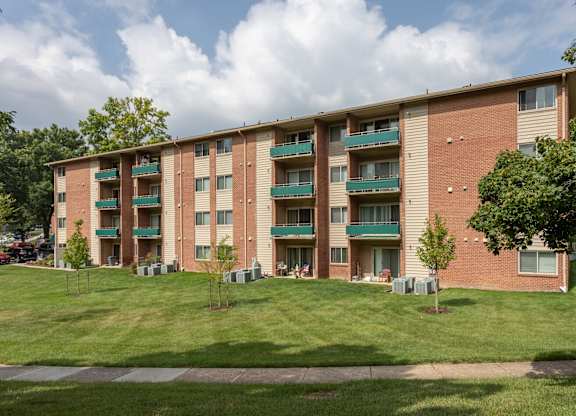 A large brick apartment building with green balconies and lawns in front.