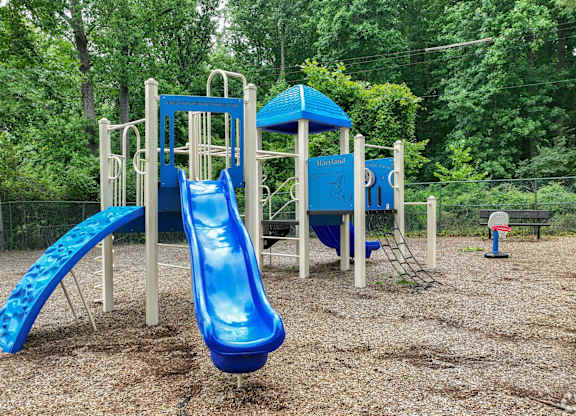 A blue slide in a playground surrounded by trees.