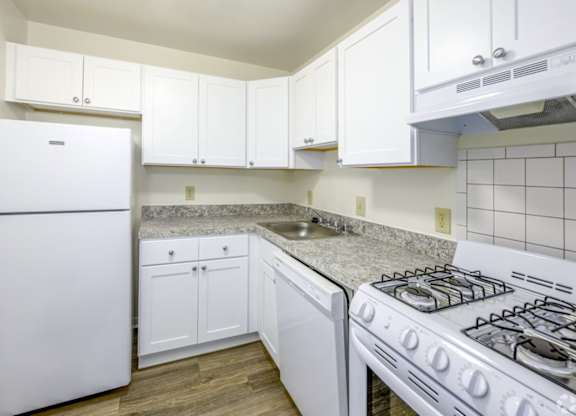 A white kitchen with a stove, sink, and cabinets.