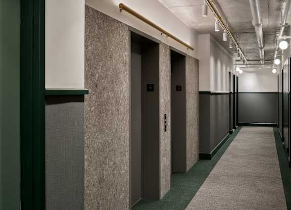 a row of elevators in a hallway with concrete walls and green carpet