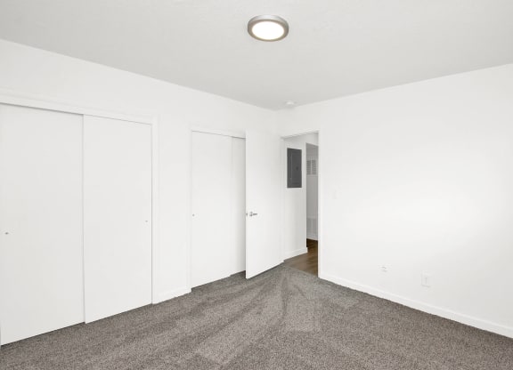 a bedroom with white walls and carpet and white closets