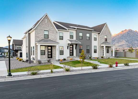 A large, modern house with a grey roof and white walls, surrounded by a well-maintained lawn and a clear sky above.