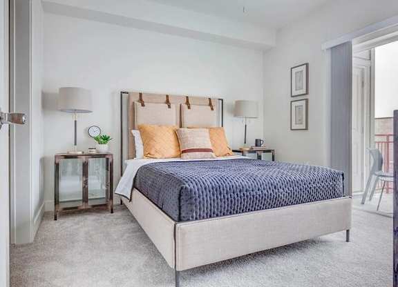 A bedroom with a large bed and a small table with a lamp.