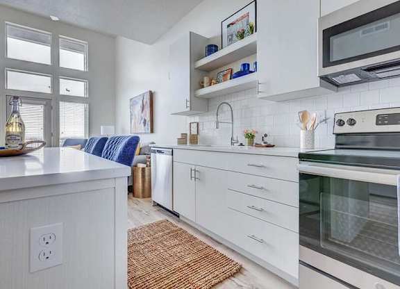 A modern kitchen with white cabinets and a blue cushion on the counter.