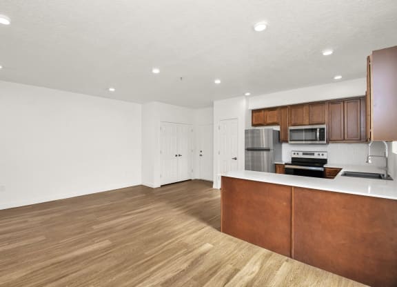 an empty living room and kitchen with wood flooring and white walls