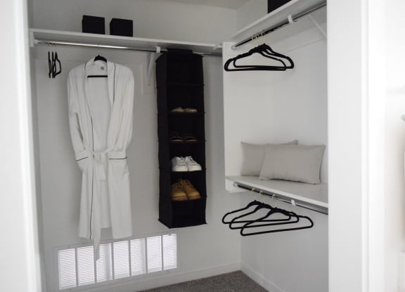 a walk in closet with a white robe and a shelf with shoes and a pillow