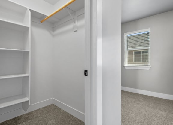 the closet in a bedroom with white shelves and a window