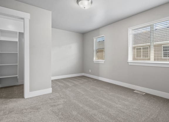 an empty living room with two windows and a door to a closet