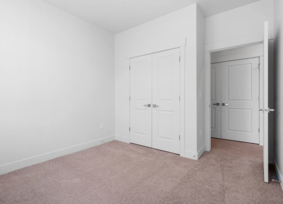 a bedroom with white walls and carpet and two doors