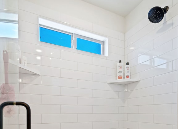 a white tiled bathroom with a shower and a window