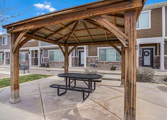 A wooden pergola with a black picnic table is in front of a building.