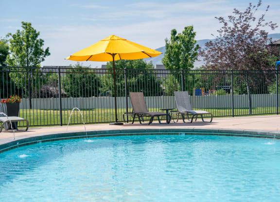 our resort style swimming pool is next to our patio with chairs and an umbrella at Aldara Apartments in Saratoga Springs, Utah