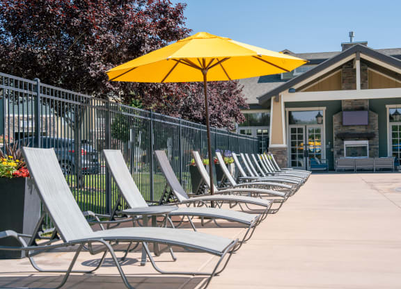 a row of lounge chairs under an umbrella in front of a building at Aldara Apartments in Saratoga Springs, Utah