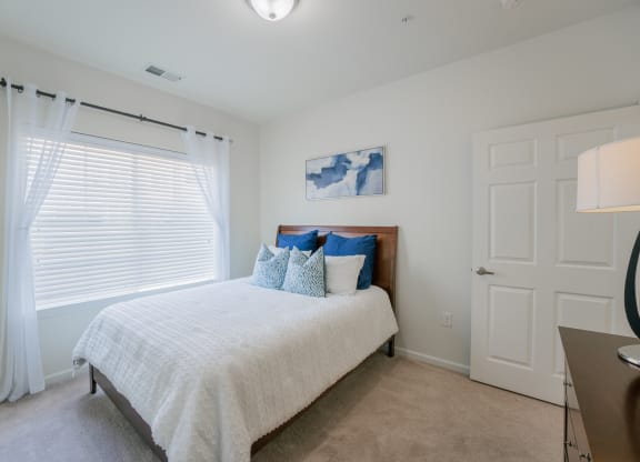 a bedroom with white walls and a bed with blue and white pillows at Aldara Apartments in Saratoga Springs, Utah