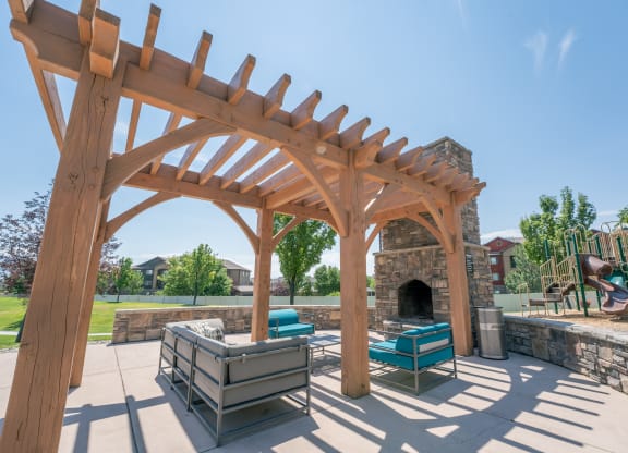 a wooden pergola with a stone fireplace and a patio with furniture at Aldara Apartments in Saratoga Springs, Utah