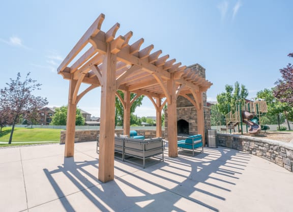 a wooden pergola over a patio with a stone fireplace at Aldara Apartments in Saratoga Springs, Utah