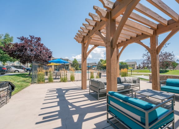 a patio with couches and a picnic table under a wooden pavilion at Aldara Apartments in Saratoga Springs, Utah