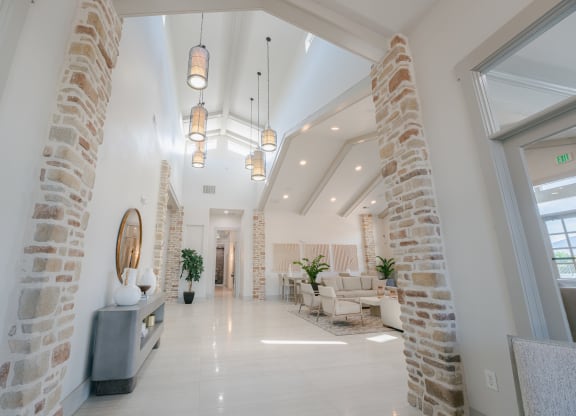 the lobby of a building with brick pillars and a reception area with chairs and tables at Aldara Apartments in Saratoga Springs, Utah