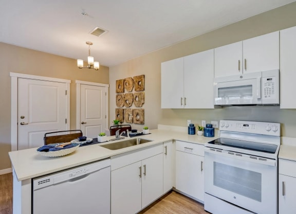 a bright and modern kitchen with white cabinets and appliances and a sink at Brookfield Apartments for rent in St. George, UT.