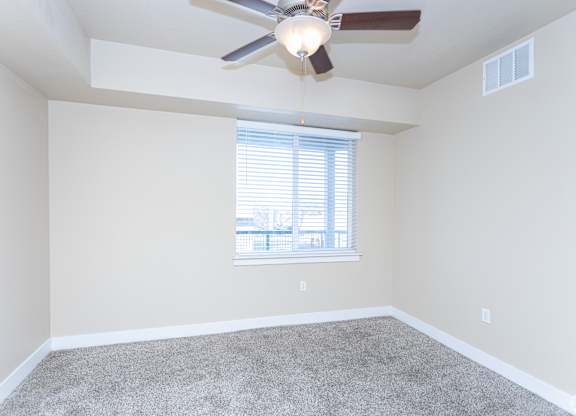 A room with a ceiling fan and a window with blinds.