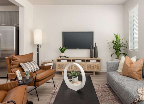 A living room with a grey sofa, a brown chair, a black coffee table, a flat screen TV, and a wooden cabinet.
